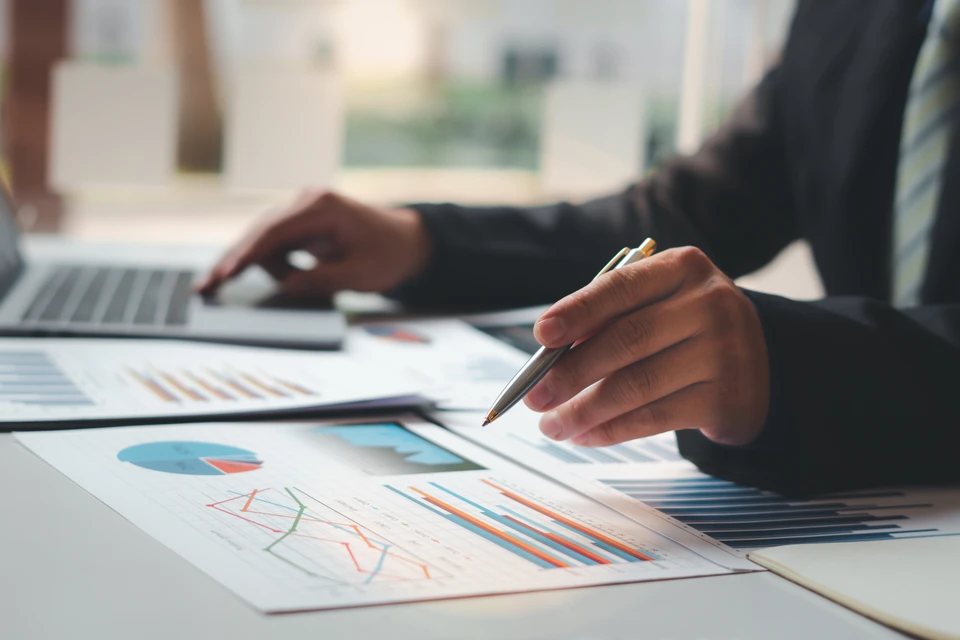 Professionnel en costume travaillant à un bureau avec ordinateur portable, analysant des documents financiers et graphiques imprimés